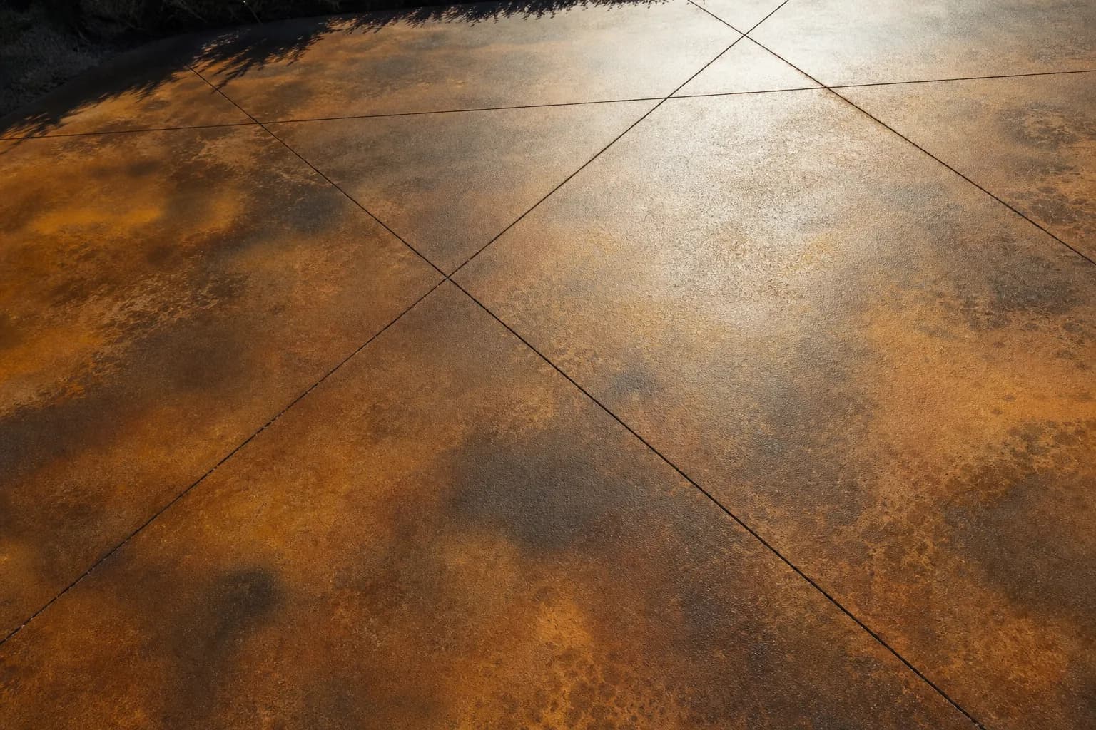 Textured and acid-stained concrete patio surface in mottled amber and brown with a saw-cut diamond pattern