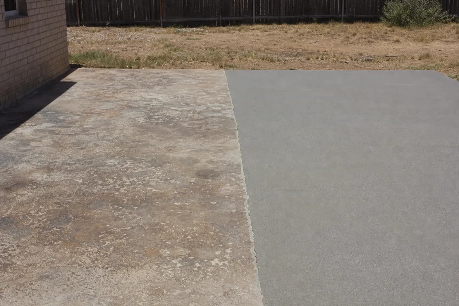 Worn, stained concrete patio half covered with a fresh smooth gray overlay, showing a sharp line between old and new
