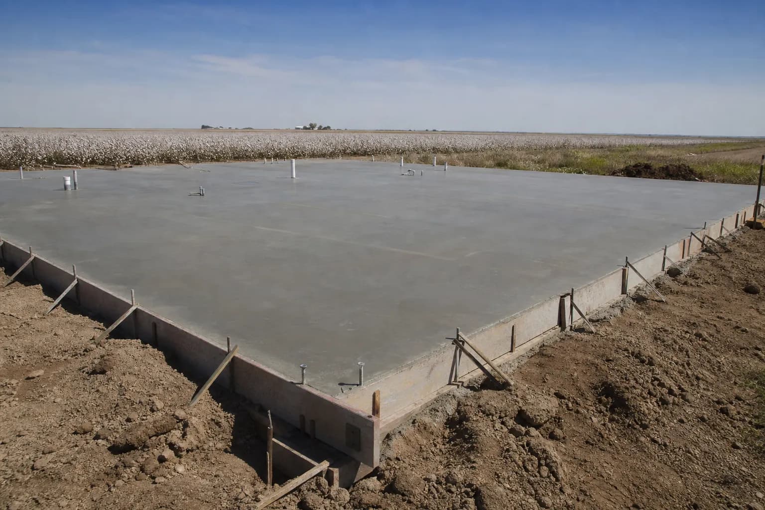 Freshly poured concrete slab for a shop building on open farmland, with wooden forms still in place along the edges