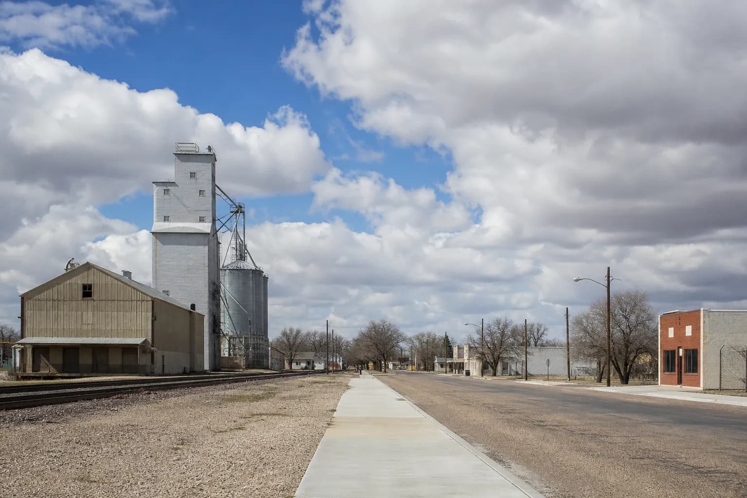 Small West Texas railroad town with a grain elevator by the tracks and a new concrete sidewalk along the street